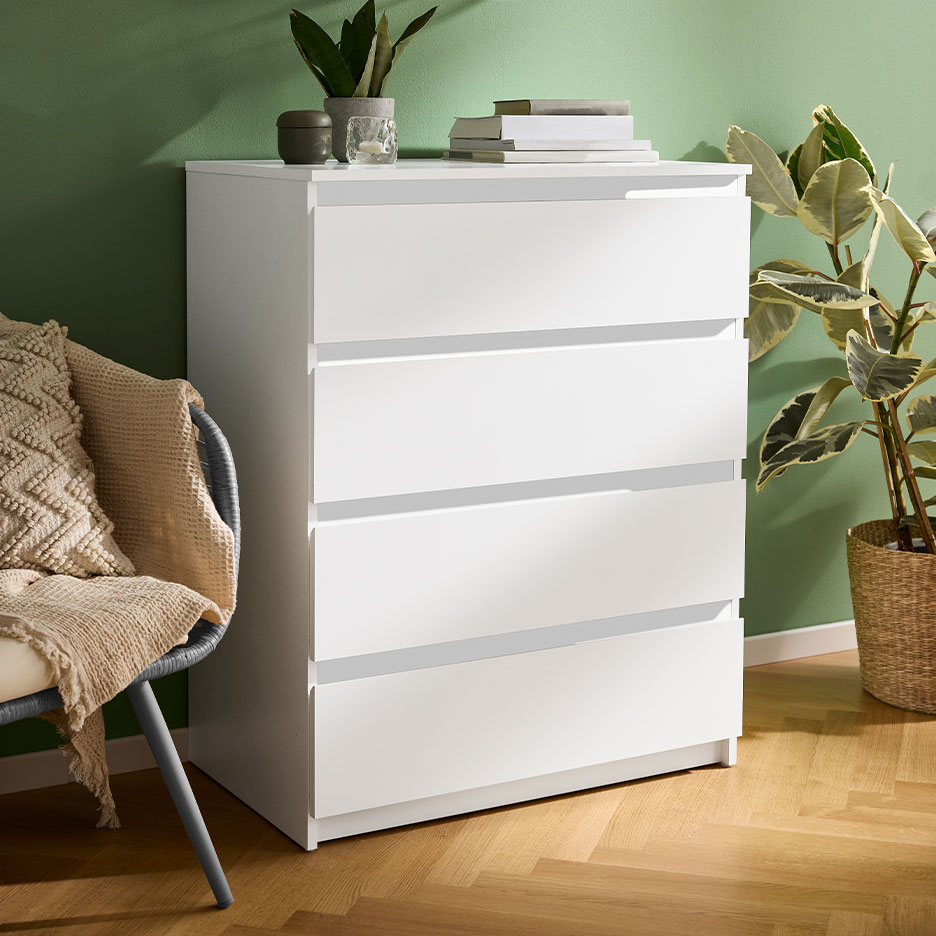Witte ladekast met vier laden in een kamer met groene muren en een houten vloer.