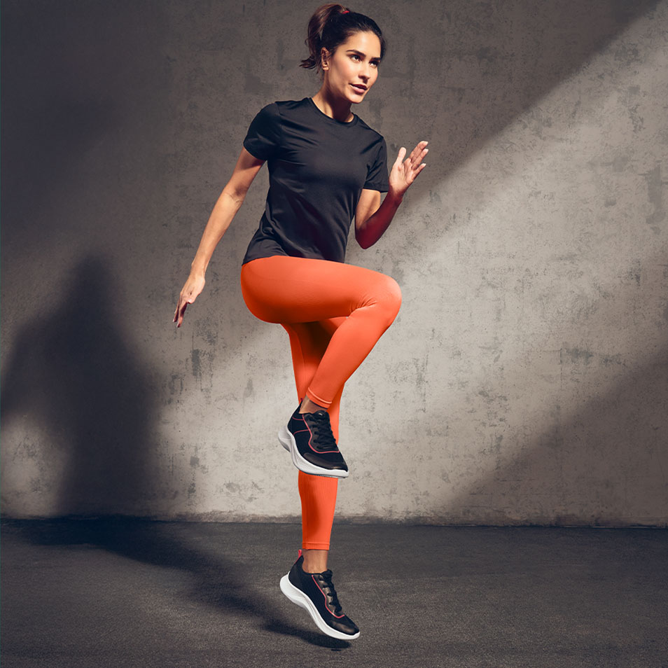 Vrouw in zwart T-shirt en oranje legging sportend in een sportschool.