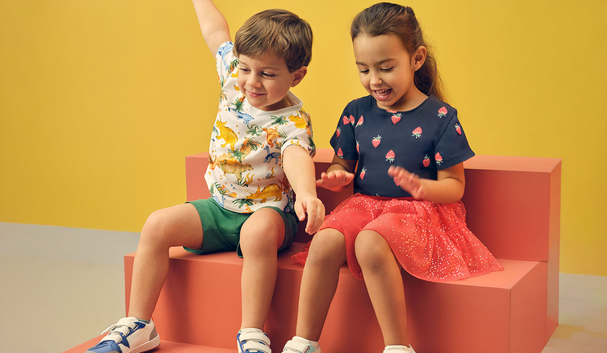 Deux enfants en vêtements d'été, un garçon en t-shirt dinosaure et une fille en t-shirt fraise.