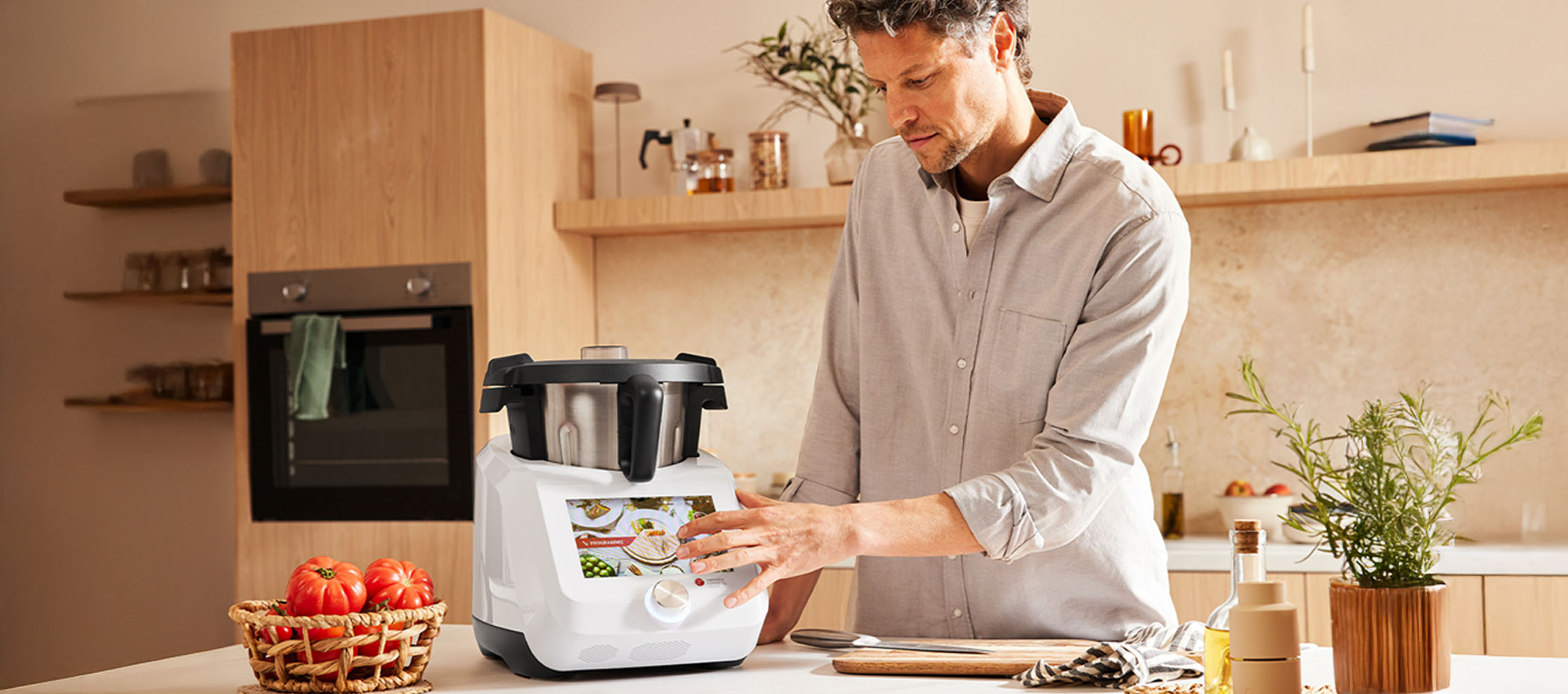 Un homme utilise un robot de cuisine intelligent blanc Silvercrest Monsieur Cuisine dans une cuisine moderne.