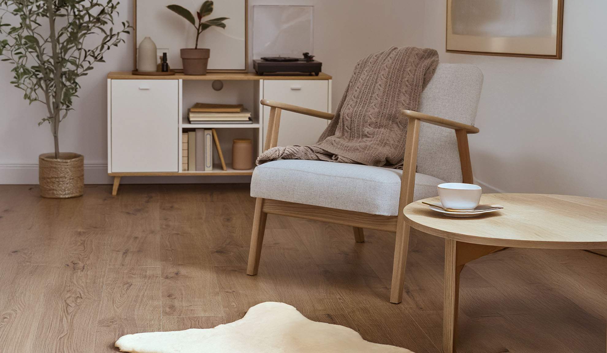 Comfortabele fauteuil met plaid, houten salontafel en opbergkast in een lichte woonkamer.