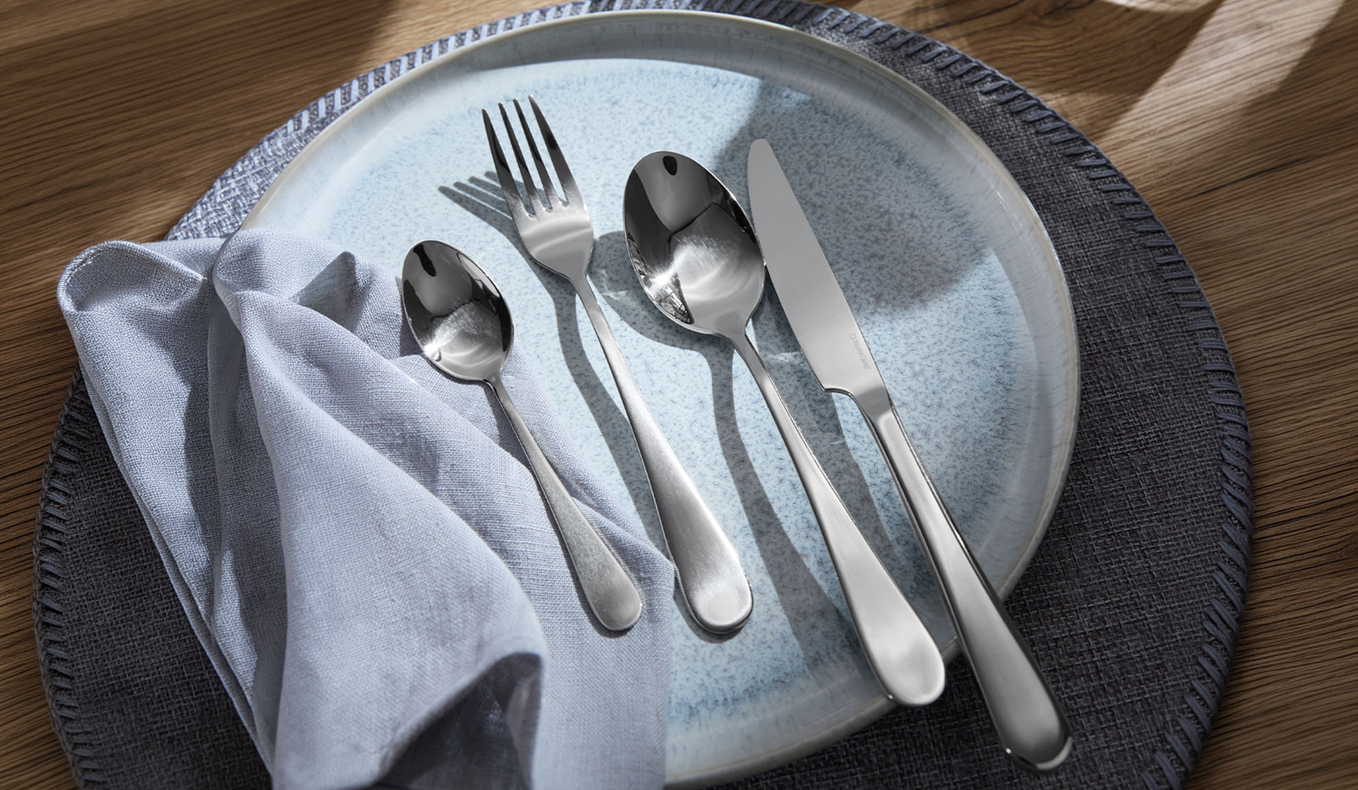 Zilverkleurig bestek op een blauw bord, met servet en placemat.