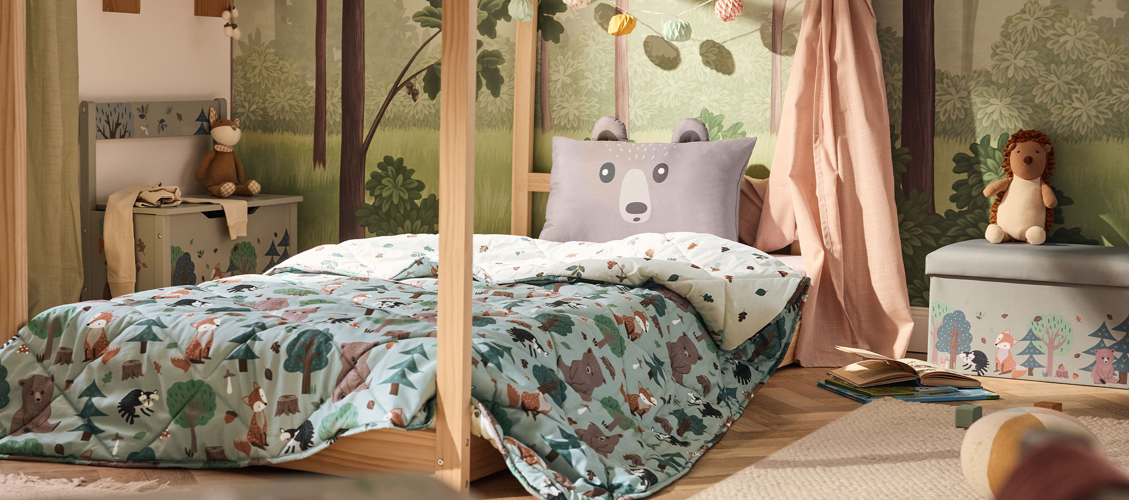 Chambre d'enfant avec lit en bois, oreiller ours et couette à motif forêt.