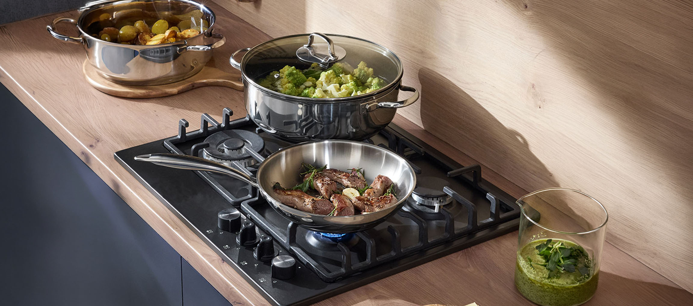 Table de cuisson à gaz avec casseroles et poêles en acier inoxydable remplies de légumes et de viande.