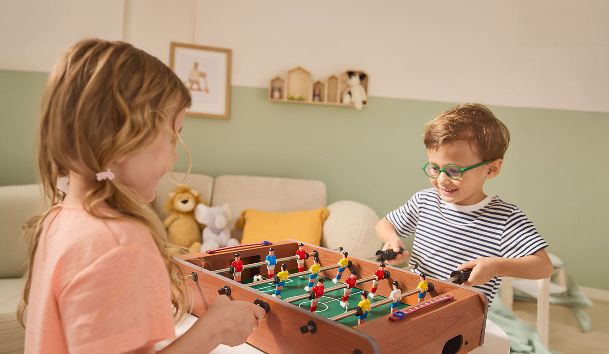 Twee kinderen spelen tafelvoetbal, vrolijk lachend.
