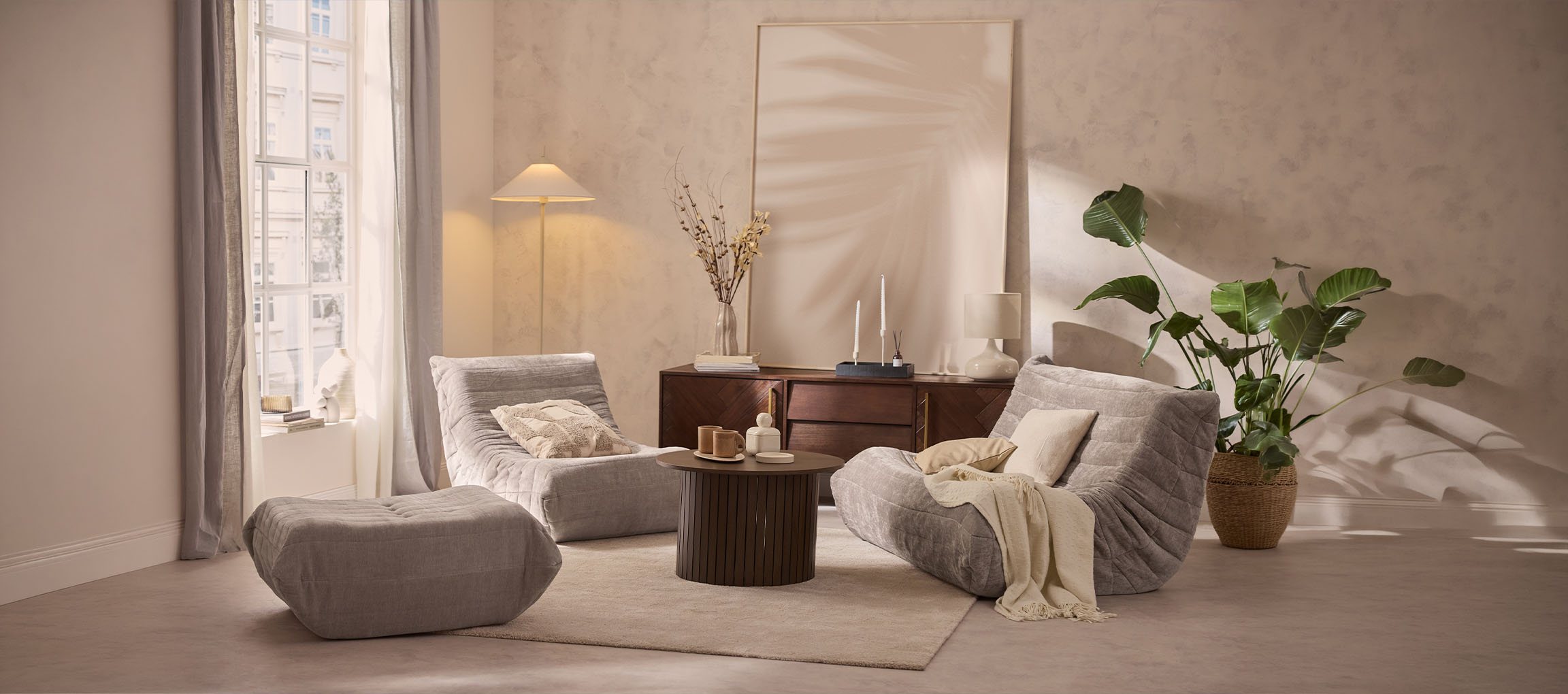 Gezellige woonkamer met twee grijze loungefauteuils, een poef en een houten tafel.