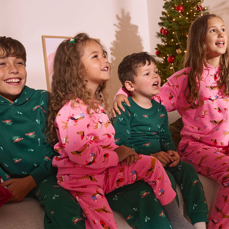 Vier kinderen in kerstpyjama's met honden- en autopatronen, zittend voor een kerstboom.