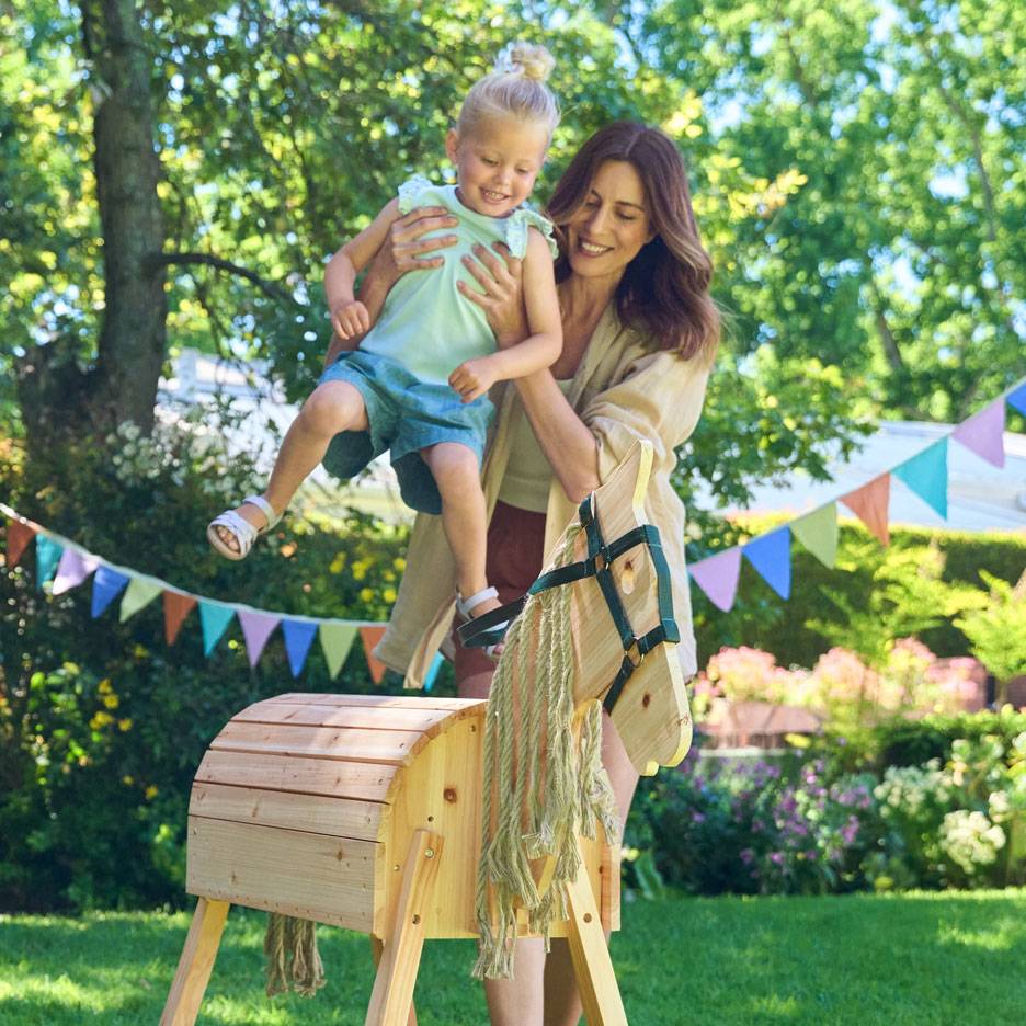 Vrouw en kind met houten hobbelpaard in tuin met slingers.
