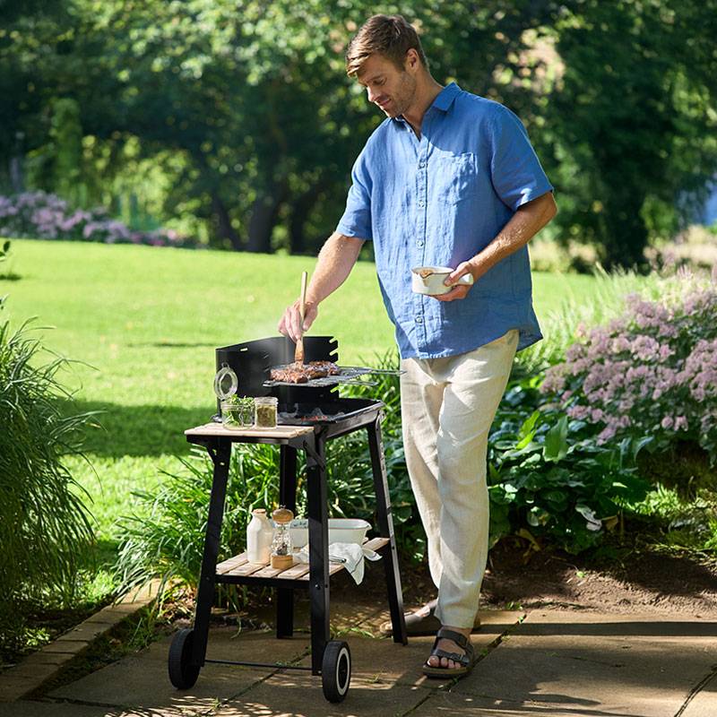Man grilt biefstuk op een barbecue in de tuin.