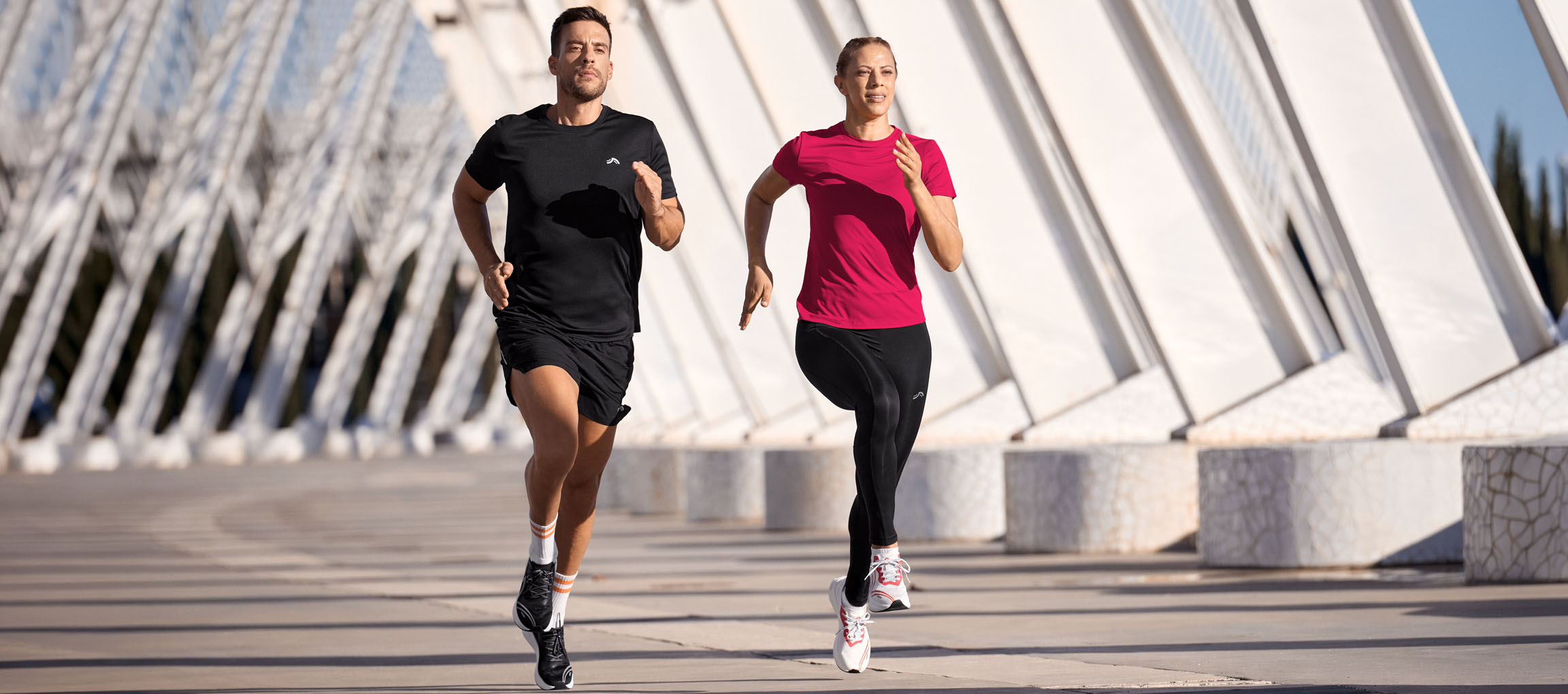 Homme et femme courant en tenue de sport, hauts noirs et roses, shorts et leggings noirs.