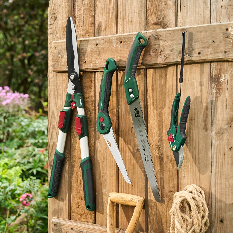 Outils de jardin Parkside: sécateur, scies et cisaille, sur un mur en bois.