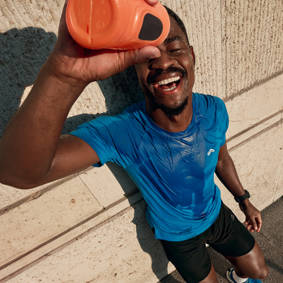 Man in blauw sportshirt en zwarte korte broek giet water over zichzelf na het sporten.
