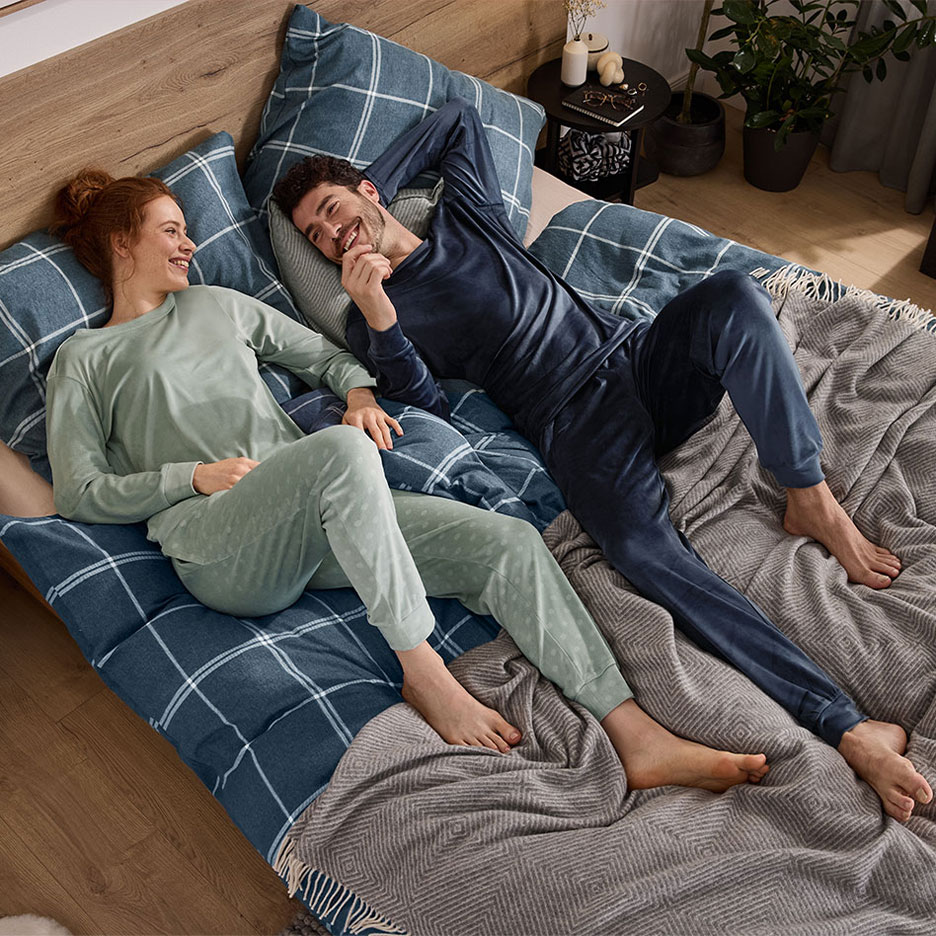 Paar in pyjama ligt op bed met geruit beddengoed en deken.