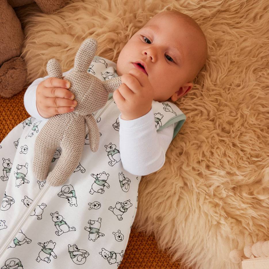Baby in witte slaapzak met berenpatroon, houdt een gebreid konijntje vast.