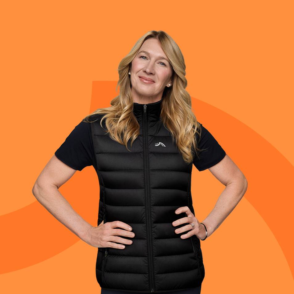 Vrouw in een zwarte bodywarmer en T-shirt, glimlachend tegen een oranje achtergrond.