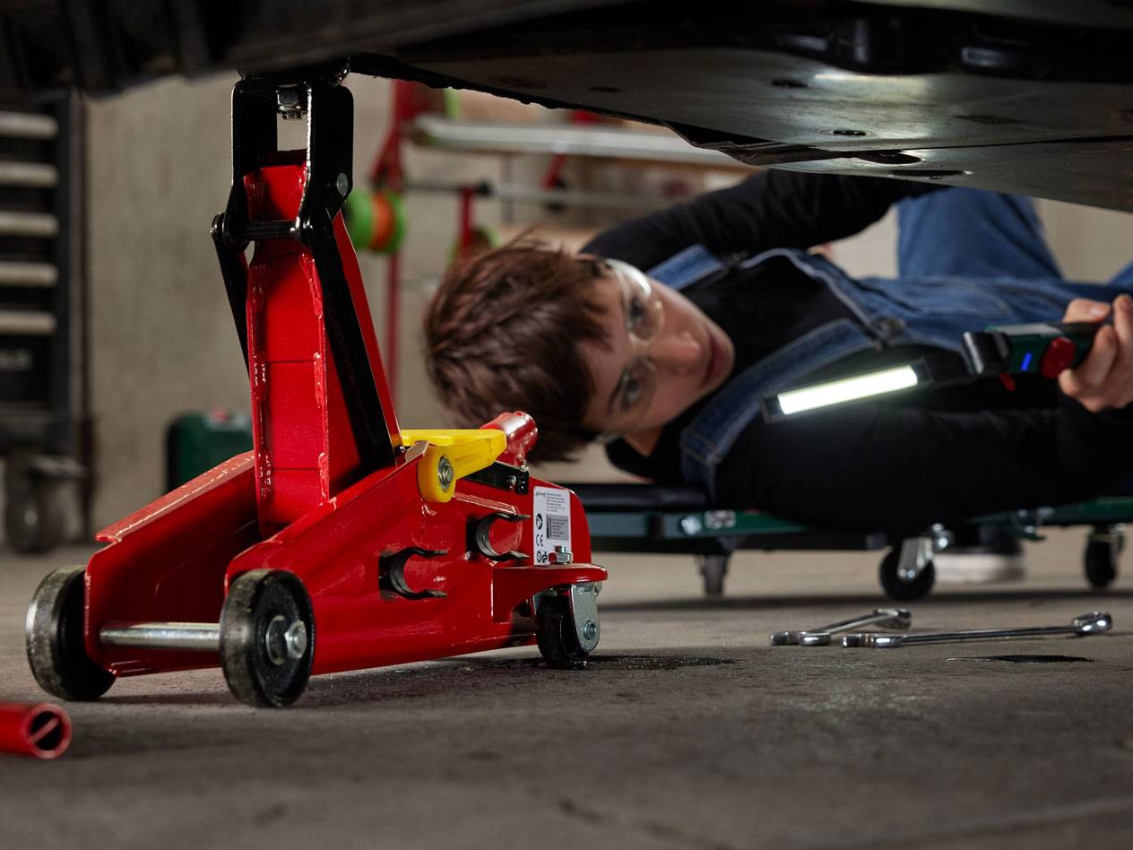 Rode hydraulische krik en vrouw onder een auto met werklamp en gereedschap.