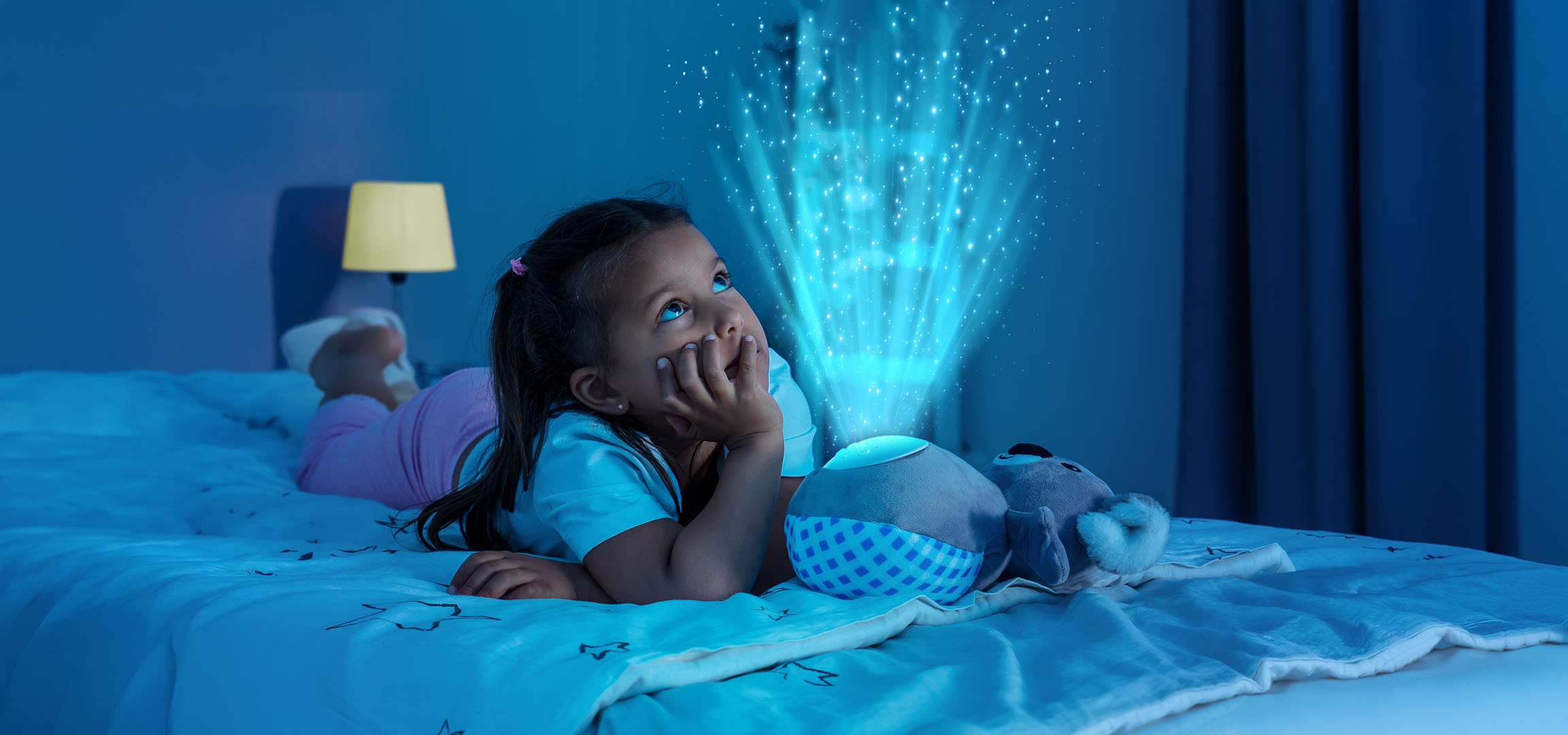 Meisje ligt in bed, kijkend naar een sterrenprojector die licht op de muur werpt.