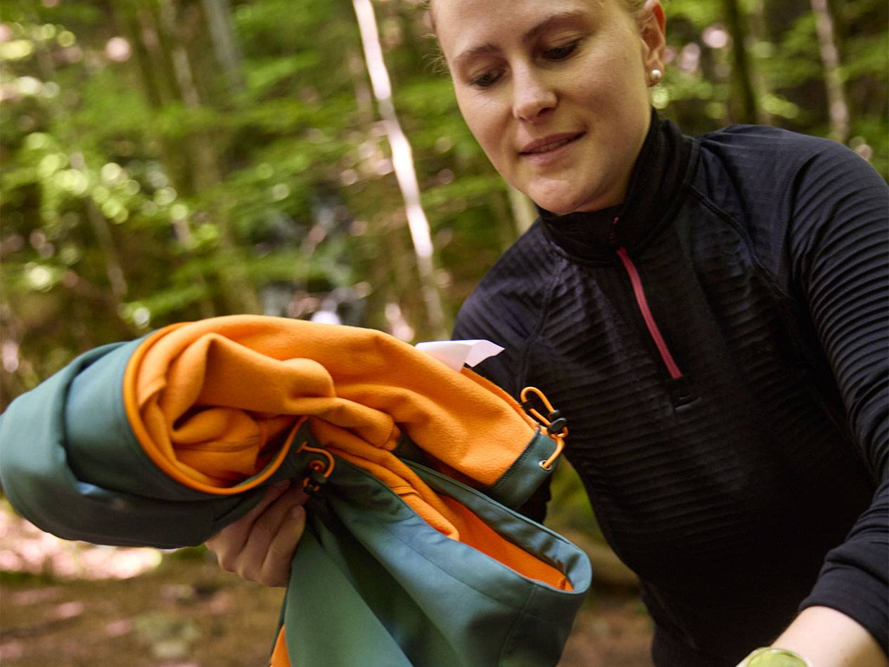 Femme dans une forêt pliant une veste de sport.