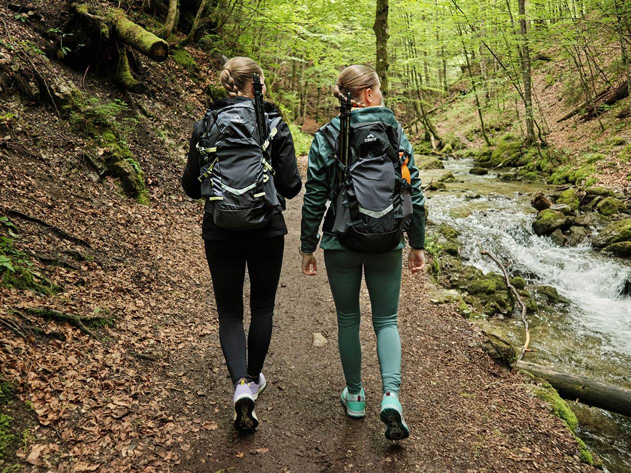Deux femmes avec des sacs à dos Crivit font de la randonnée sur un sentier forestier.