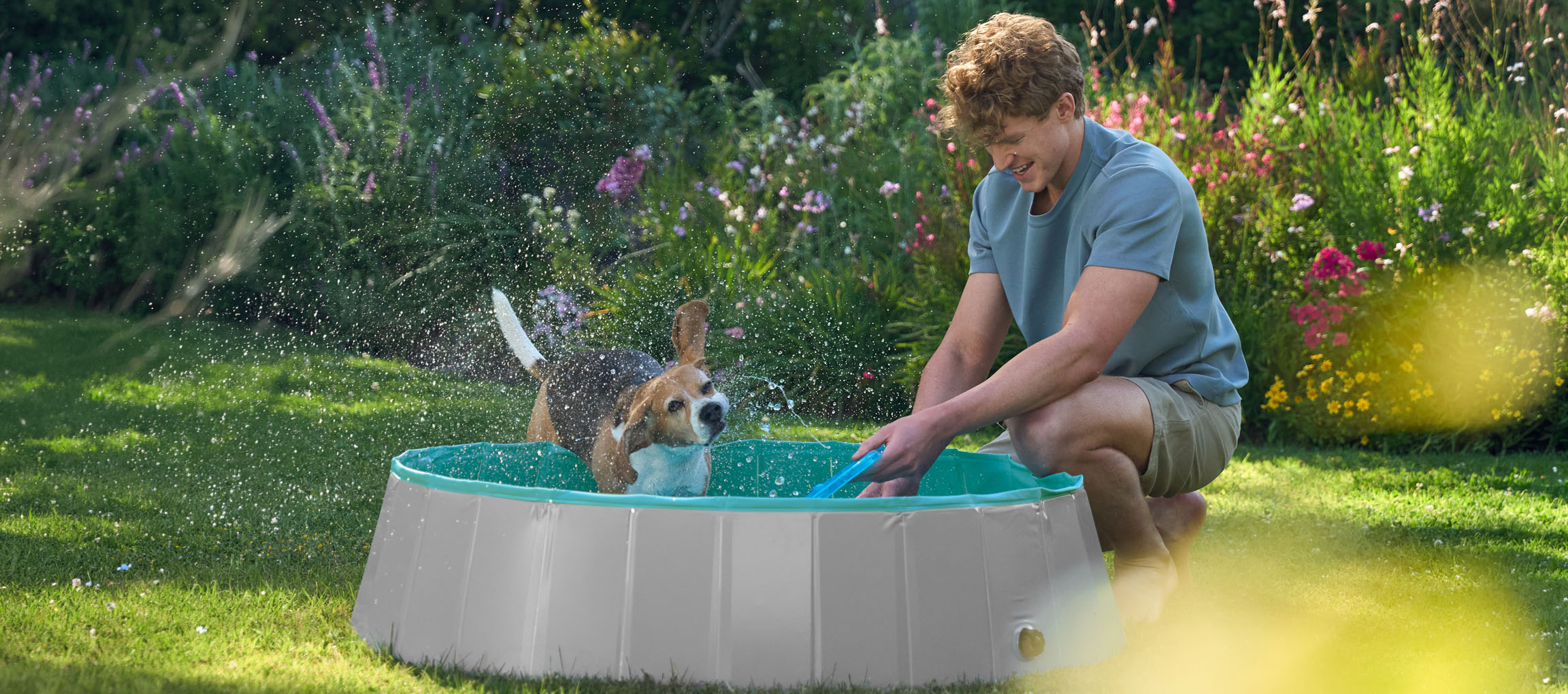 Man en hond spelen in een kinderzwembad in de tuin.